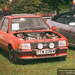 Red prototype Ford Escort XR3 displayed on grass at Oulton Park with its bonnet removed, showing the engine bay