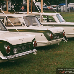 Three white and green Lotus Cortinas lined up beneath a display structure at Oulton Park